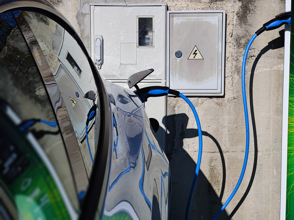 EV Car or Electric Vehicle at Charging Station with the Power Cable Supply Plugged in on Blurred Nature with Blue Enegy Power Effect. Eco-Friendly Sustainable Energy Concept.